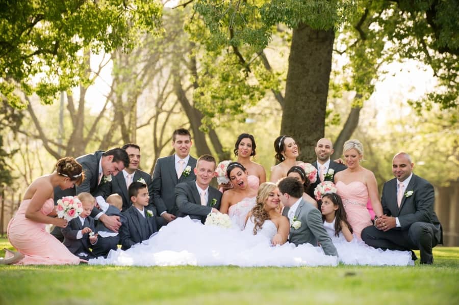 Happy wedding party posing in sunlit garden park with bride centerpiece.